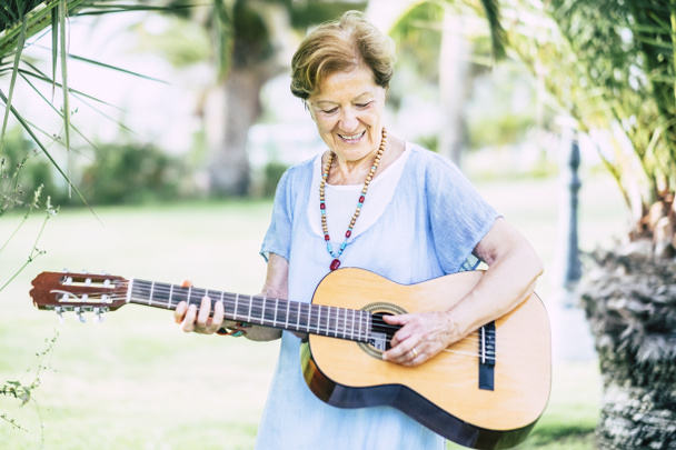Wesoły i szczęśliwy stary wiek starszy kaukaski kobieta uśmiecha się i zabawy gry na gitarze i dong muzyki w outdoor park rozrywki - Zdjęcie, obraz