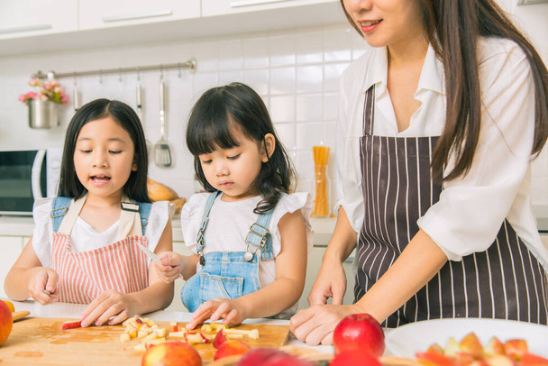 Дівчинка насолоджується грою нарізаного яблука разом з матір'ю і сестрою на домашній кухні
. - Фото, зображення