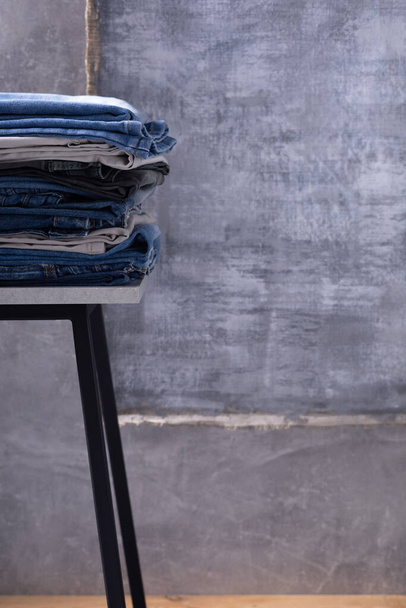 Denim jeans at shelf or stool. Stack of jeans near abstract background texture surface - Foto, afbeelding