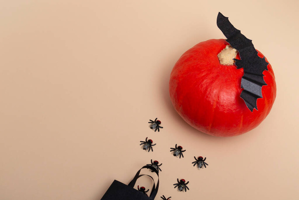 Draufsicht auf einem beigen Hintergrund schwarzes Paket mit Fliegen, Kürbis und Fledermäusen. Nahaufnahme einer Halloween-Party. Einladungslayout. Banner - Foto, Bild