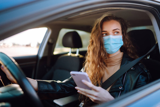 Young woman driving a car wearing on a medical mask during an epidemic. Transport isolation. Covid-2019. - Foto, imagen
