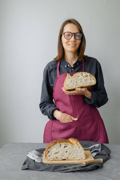 yeast-free sourdough bread. a beautiful European woman baker holds bread in her hands - Фото, изображение