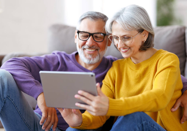 Όμορφο ώριμο οικογενειακό ζευγάρι κοιτάζοντας tablet με χαμόγελο στο πρόσωπο, ενώ περνούν το χρόνο τους μαζί - Φωτογραφία, εικόνα