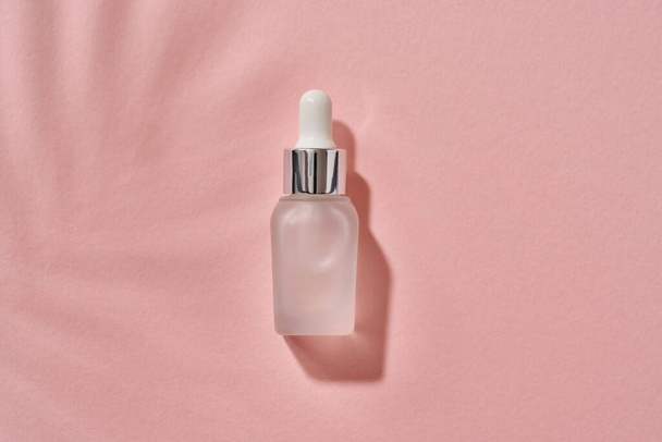 Uma garrafa de óleo essencial de aromaterapia em um fundo rosa pastel com uma sombra de folhas de palma - Foto, Imagem