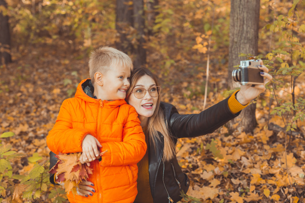 Poika ja äiti ottavat selfien kameralle syyspuistossa. Yksinhuoltaja-, vapaa-ajan- ja syyskauden käsite. - Valokuva, kuva