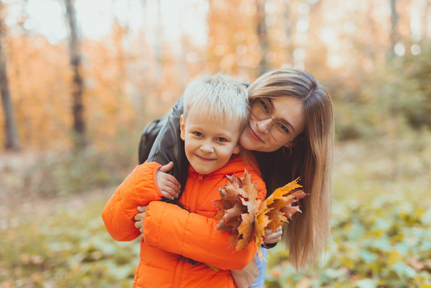 Mother hugging her child during walk in autumn park. Fall season and single parent concept. - Photo, image