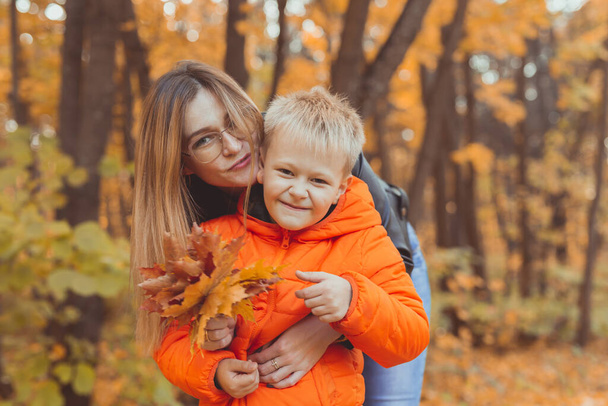 Mother hugging her child during walk in autumn park. Fall season and single parent concept. - Foto, Bild