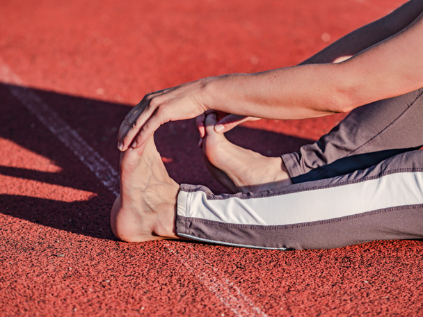 Vorbeugende Übungen gegen Krämpfe und Verletzungen von Sehnen und Muskeln. Sportlerin streckt sich vor Lauf barfuß.  - Foto, Bild