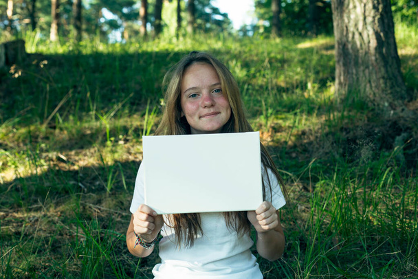 白い紙を持っているティーンの女の子(あなたのメッセージのために) 、公園で. - 写真・画像