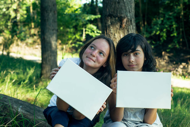 公園にきれいな白い紙(あなたのメッセージのためのバナー)を持っている2人の友人のテニール.  - 写真・画像