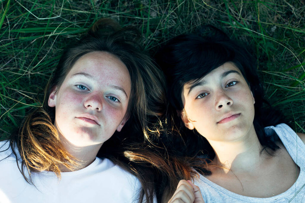 Retrato de dos amigas tumbadas en la hierba verde del parque. - Foto, Imagen