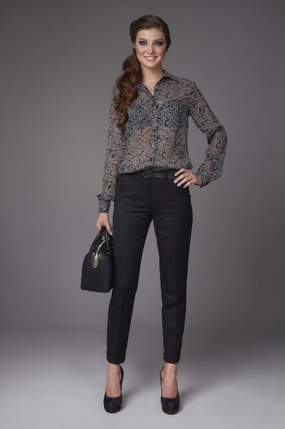 Beautiful sexy young business woman with evening makeup dressed in tight pants silk blouse with lace long sleeves high-heeled shoes and a small black handbag, business clothes for meetings and walks - Foto, immagini