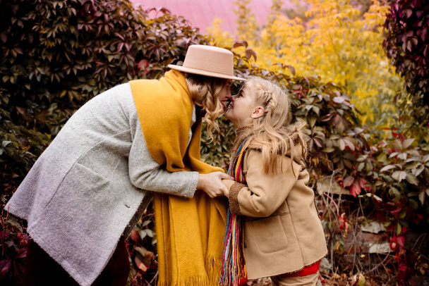 A young adult blonde mother with a 7-year-old daughter on a walk in the autumn park hug and laugh - Fotó, kép