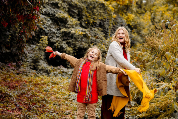 A young adult blonde mother with a 7-year-old daughter on a walk in the autumn park hug and laugh - Фото, зображення