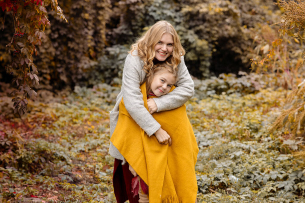 Молодая взрослая блондинка мать с 7-летней дочерью на прогулке в осеннем парке обнимаются и смеются - Фото, изображение
