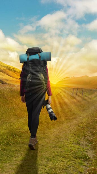 Kaunis latinonainen tutkimusmatkailija takaa nähtynä reppu selässä kävellen kamera kädessä keskellä kylvettyä peltoa pilvisenä aamuna. - Valokuva, kuva