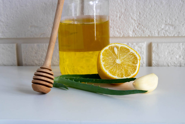 Composition with natural cold remedies on a white table on a yellow background. Garlic, honey, lemon, aloe folk remedies for autumn colds, covida. - 写真・画像