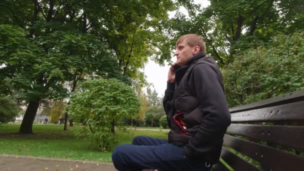 Ο άνθρωπος μιλάει στο τηλέφωνο σε ένα παγκάκι - Πλάνα, βίντεο