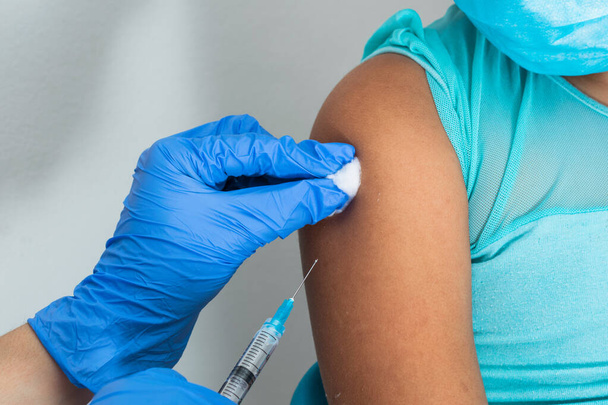 children's nurse wiping blood with cotton wool after administering injection in brown girl's arm. doctor injecting vaccine against covid-19. flu vaccine. medical concept, health and pandemic. - Фото, изображение