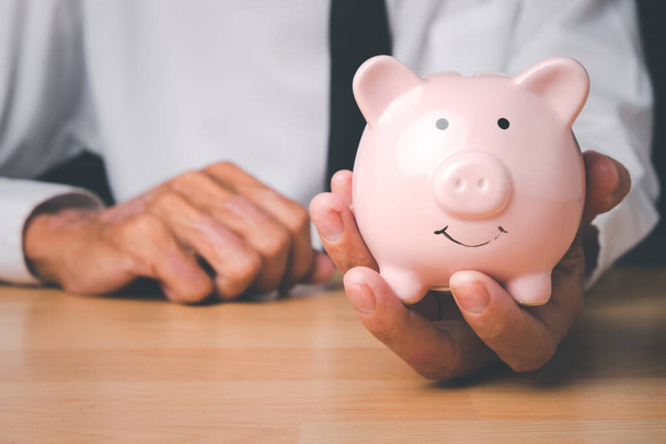 Man hand holding piggy bank on wood table, Concept financial business investment, business, finance, investment, financial planning. - Foto, Imagem