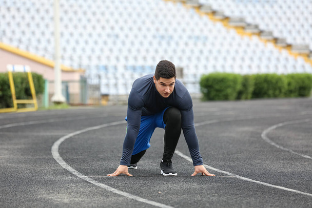 Musculoso joven preparándose para correr en el estadio - Foto, imagen