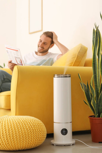 Young man reading newspaper in room with modern humidifier - Foto, Imagem