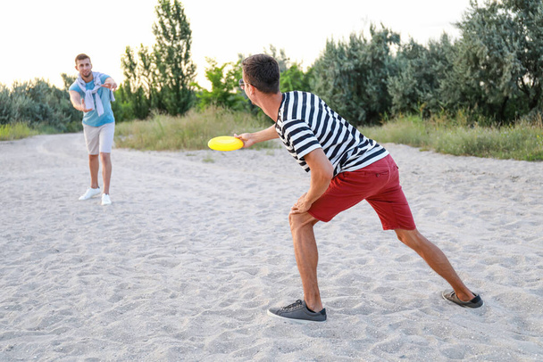 Młodzi mężczyźni grający frisbee na plaży morskiej - Zdjęcie, obraz