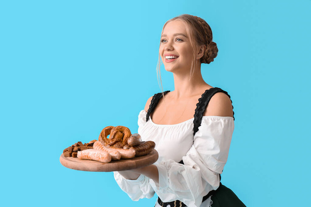 Schöne Frau in traditioneller deutscher Tracht und mit Snacks auf farbigem Hintergrund - Foto, Bild