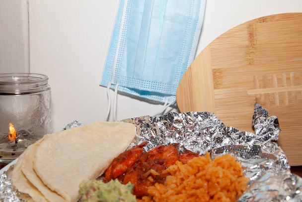 Camarão picante quente em folha ao lado de tortilhas de milho dobradas, arroz e guacamole, wih uma vela, duas máscaras de papel, e uma bola de futebol de madeira no fundo - Foto, Imagem