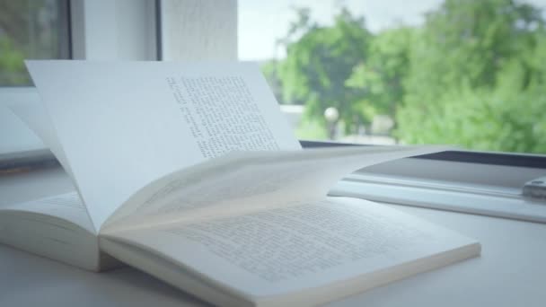 Egy nyitott lapos könyv fekszik egy nyitott ablak ablakpárkányán, a nap sugarai a lapokon. - Felvétel, videó