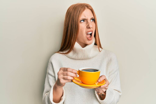 Young irish woman drinking a cup of coffee angry and mad screaming frustrated and furious, shouting with anger. rage and aggressive concept.  - Foto, Imagen