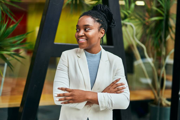 Młoda afrykańska bizneswoman uśmiecha się szczęśliwa z ramionami skrzyżowanymi w mieście. - Zdjęcie, obraz