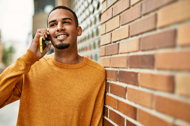 Mladý africký Američan se šťastně usmívá mluvit na smartphone ve městě. - Fotografie, Obrázek