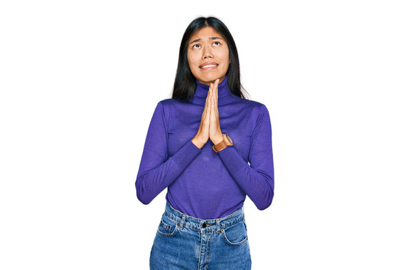 Hermosa mujer asiática joven con ropa casual mendigando y rezando con las manos junto con la expresión de esperanza en la cara muy emocional y preocupado. mendicidad.  - Foto, Imagen