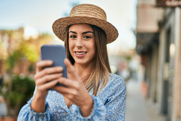 Joven mujer hispana sonriendo feliz usando smartphone en la ciudad - Foto, imagen