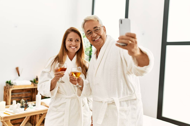 Středověký hispánský pár pije šampaňské, aby selfie u smartphonu ve wellness centru. - Fotografie, Obrázek