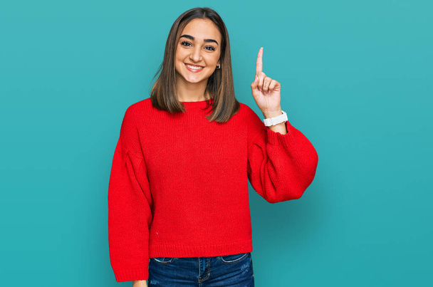 Beautiful brunette woman wearing casual winter sweater showing and pointing up with finger number one while smiling confident and happy.  - Photo, Image