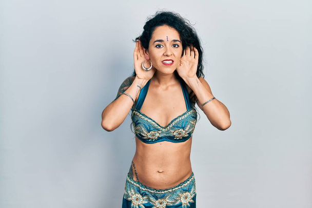 Young woman wearing bindi and traditional belly dance clothes trying to hear both hands on ear gesture, curious for gossip. hearing problem, deaf  - Photo, Image