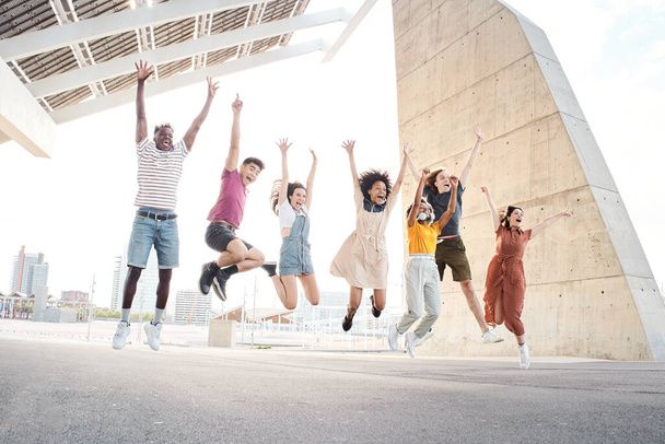 Ryhmä onnellisia monikansallisia ystäviä pitää hauskaa. Nuoret opiskelijat hyppäävät yliopiston ulkopuolella. - Valokuva, kuva
