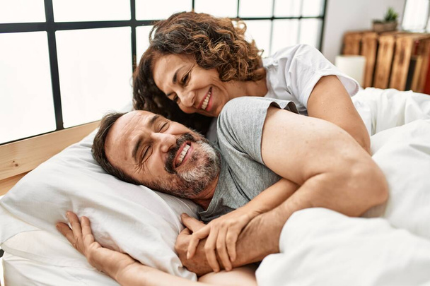 Середньовічна пара іспаномовних посміхається щасливим і обіймає лежачи на ліжку вдома
. - Фото, зображення