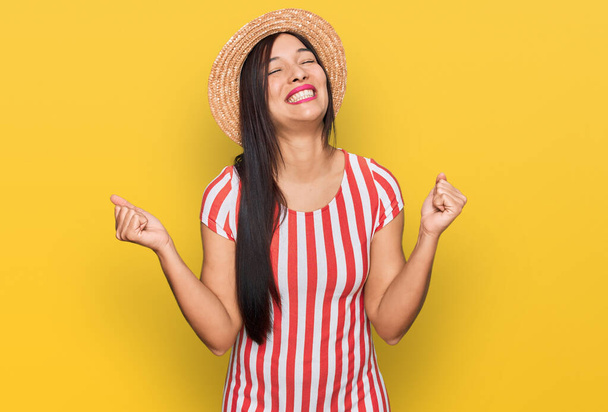 Fiatal spanyol nő visel nyári kalap nagyon boldog és izgatott csinál győztes gesztus felemelt karokkal, mosolygós és sikoltozó siker. ünnepség koncepciója.  - Fotó, kép
