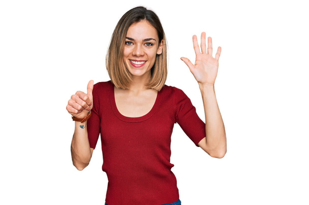 Молода блондинка в повсякденному одязі показує і вказує пальцями номер шість, посміхаючись впевнено і щасливо
.  - Фото, зображення
