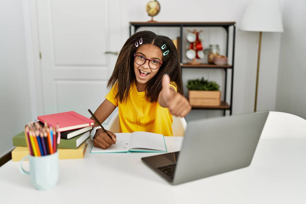 Young african american girl doing homework at home approving doing positive gesture with hand, thumbs up smiling and happy for success. winner gesture.  - Foto, Imagen