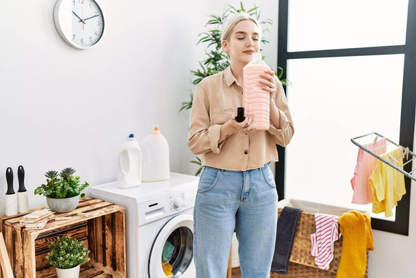 Young caucasian woman smiling confident smelling detergent at laundry room - Foto, Imagen
