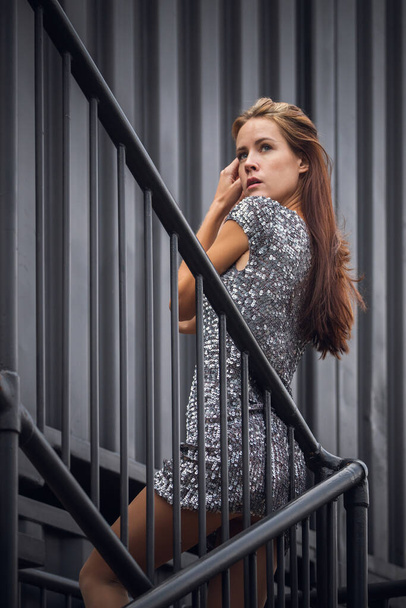 Portrait extérieur en gros plan d'une jeune belle femme en robe brillante posant contre un contenant industriel.Concept de mode. - Photo, image