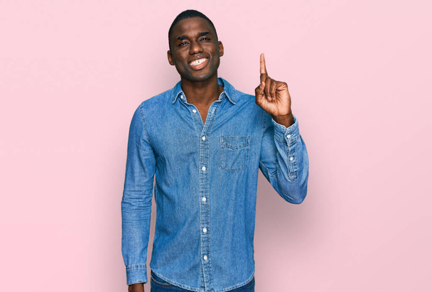 Fiatal afro-amerikai férfi, alkalmi ruhában, első számú ujjal mutogatva, magabiztosan és boldogan mosolyogva..  - Fotó, kép