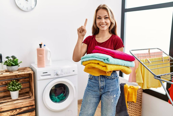 Junge kaukasische Frau mit sauberer Wäsche, die mit einer Idee oder Frage lächelt und mit glücklichem Gesicht den Finger zeigt, Nummer eins  - Foto, Bild