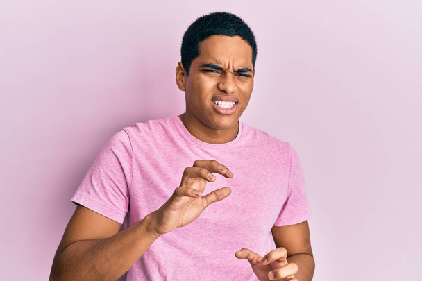Homem hispânico bonito jovem vestindo casual rosa t-shirt expressão repugnante, descontente e temeroso fazendo rosto repugnante porque reação de aversão. com as mãos levantadas  - Foto, Imagem