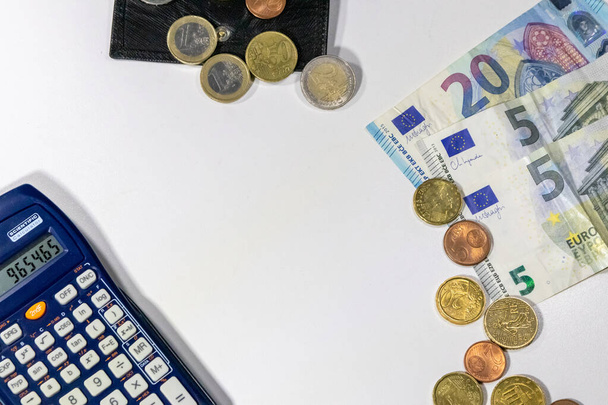 Europees geld met zwarte portemonnee op wit bureau als witte achtergrond met verschillende euromunten en eurobankbiljetten met rekenmachine voor financieel beheer en inkomstenplannen voor belastingberekening - Foto, afbeelding