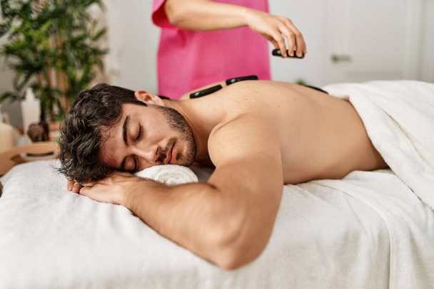 Man reciving back massage with black stones at beauty center. - Fotó, kép